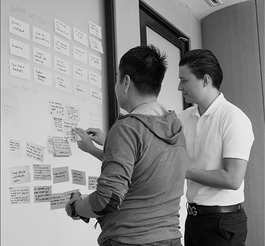 A photo of Gohan's founder Yohji Alexander Kanki leading a startup entrepreneur through a workshop board and consults the man with a new strategy in a modern meeting room and a whiteboard.